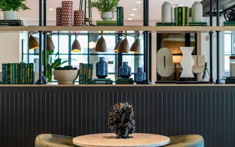 a clubhouse room with a table, chairs and a shelf with plants on it